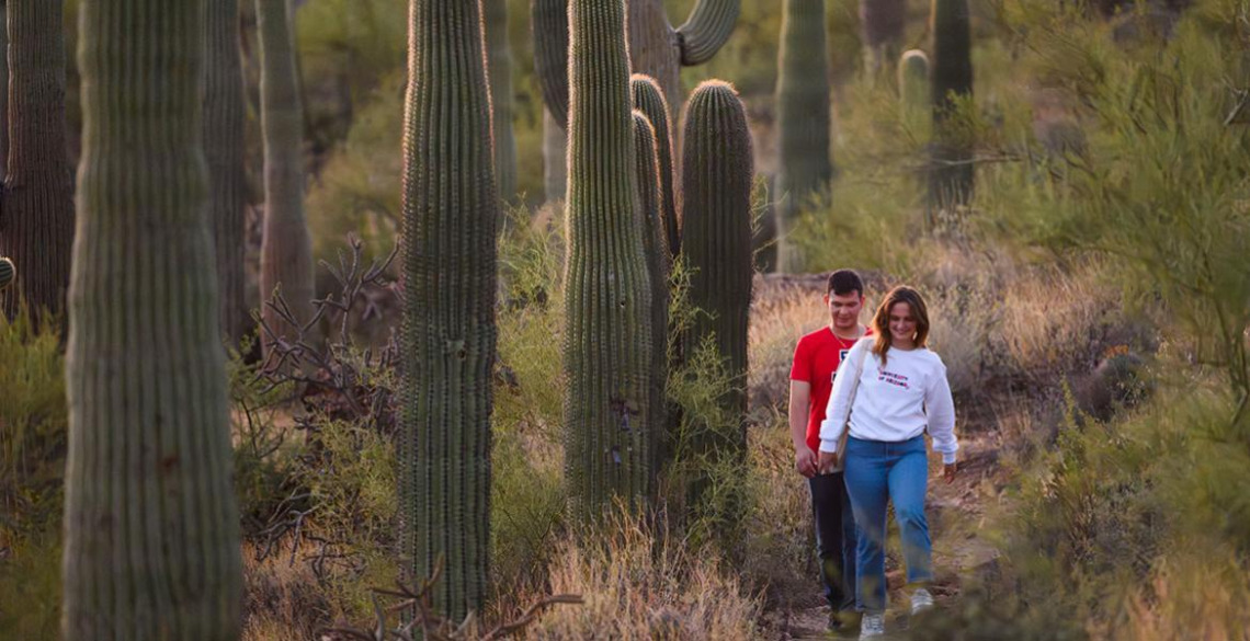 two people walking on trail with saguaro cacti