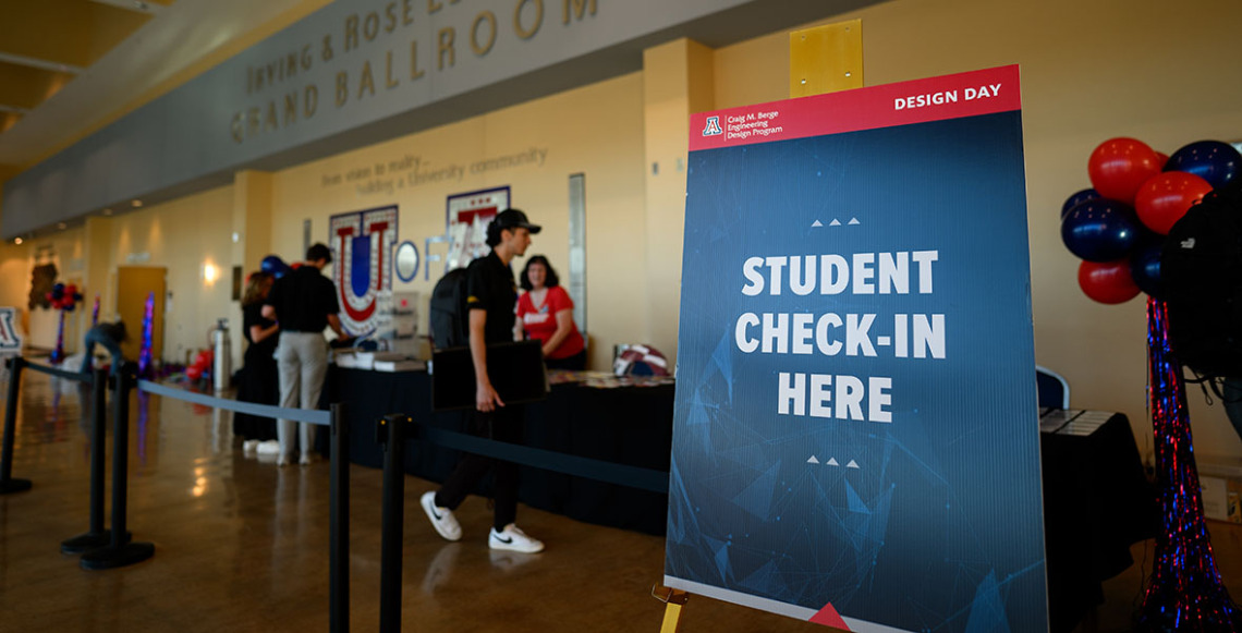 Students sign into the Design Day Open House at a booth in the yellow-toned UA ballroom.