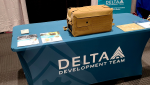 A portable refrigerator with military gear sitting on a Delta Development Team table