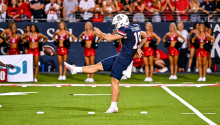 Kyle Ostendorp in full football gear kicking a football in front of a crowded stadium