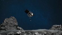 Artist's rendering of the spacecraft OSIRIS-REx, a silver body in the center, approaching Bennu, a gray asteroid body in the foreground.
