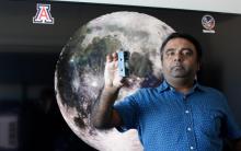 Jekan Thanga holding a small robot in his hand while standing in front of a picture of the moon