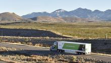 A TuSimple truck on a flat highway in the desert, with mountains in the distance.
