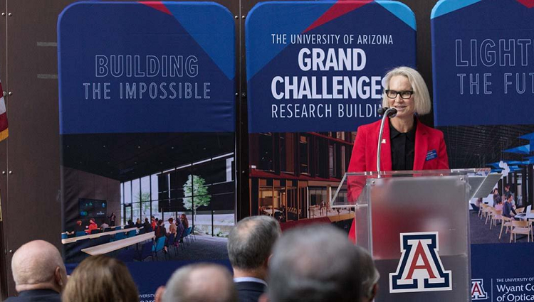 Betsy Cantwell standing at a podium, in front of a blue University of Arizona poster