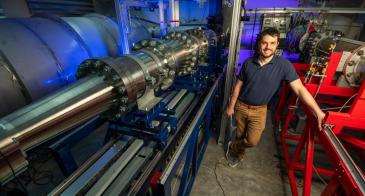 Alex Craig next to the Mach 5 wind tunnel in his lab, with blue light behind him.