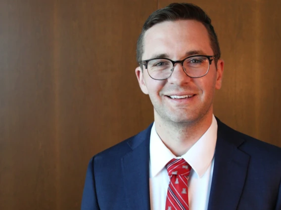 A portrait of a man with brown hair wearing a navy suit jacket and red tie.