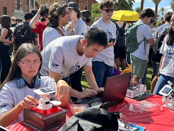 Two young people hover over a piece of technology on a grassy lawn.