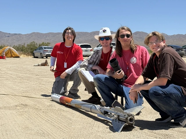 Students from the Wildcat Rocket Engineering Club pose with their rocket in the desert