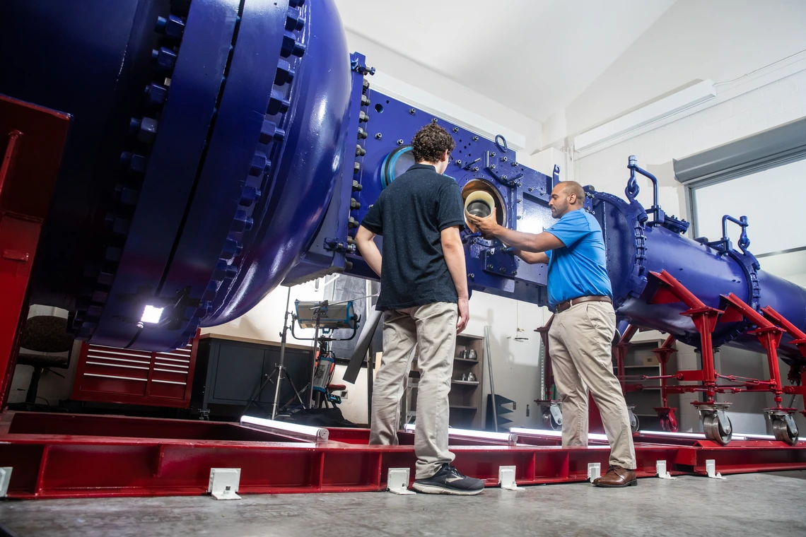 Two men handle parts of a major wind tunnel.
