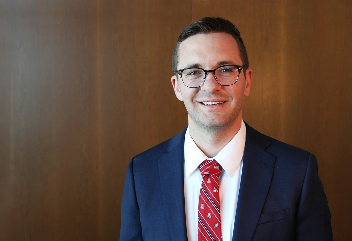 A man with brown hair poses for a photo in a blue blazer.