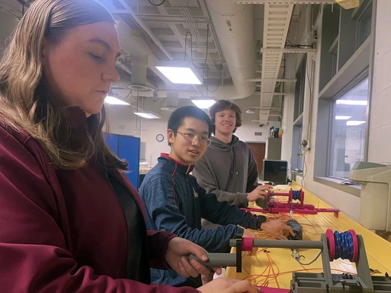 Two men and one woman test a gray and red pulley system.