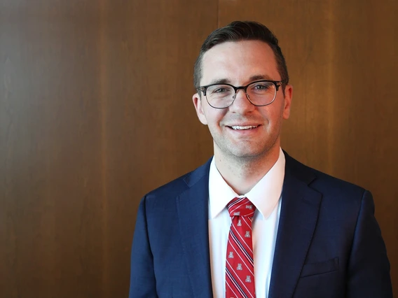 A man with brown hair poses for a photo in a blue blazer.