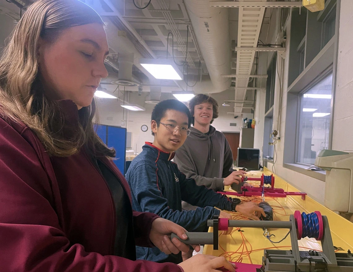 Two men and one woman test a gray and red pulley system.